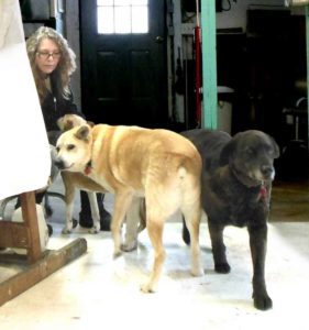 Photo of Elizabeth Lisa Petrulis in front of draped easel and withthe three dogs Sadie, Dino, and Mookie.